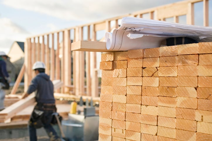 2-by-4s-stacked-with-contractor in background-on-jobsite