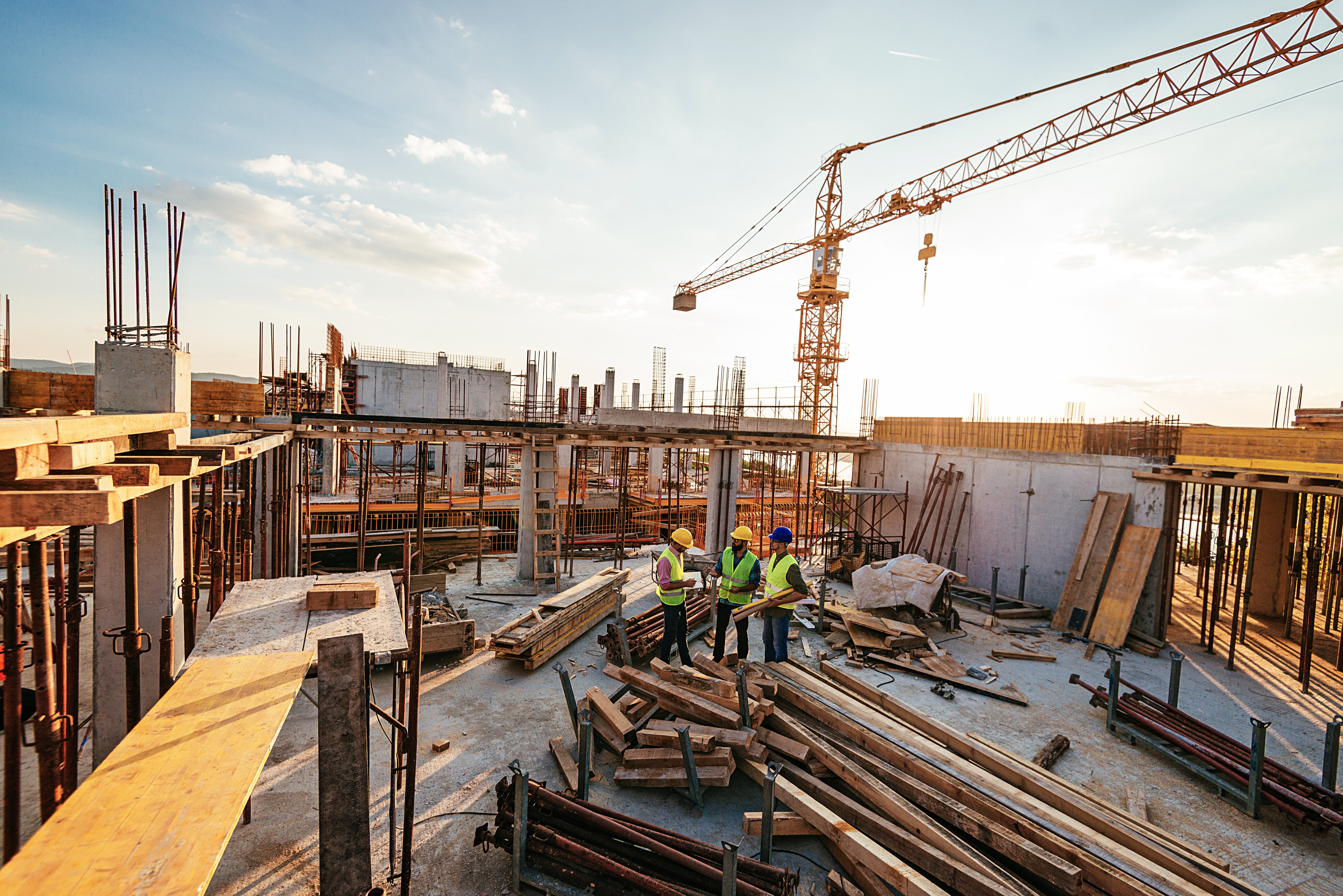 3 construction workers on site beside materials including prefabricated panels