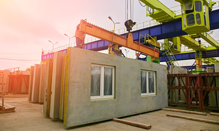 A builder installs a concrete floor slab panel at a construction site