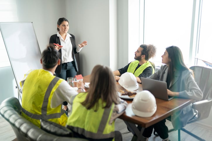 A group of construction works sit around table while being coached