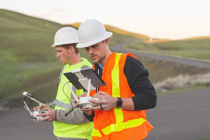 A pair of engineers use a drone to inspect wind farms and power plants