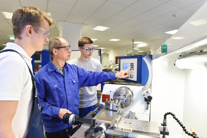 A vocational college instructor teaches two young students how to operate CNC machine