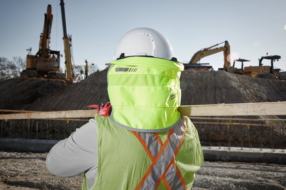 Construction worker in foreground carries 2x4 on active jobsite