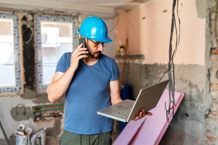Contractor on jobsite consults laptop screen while on client phone call