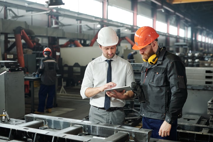 Executive in hardhat and bearded engineer discussing technical sketch