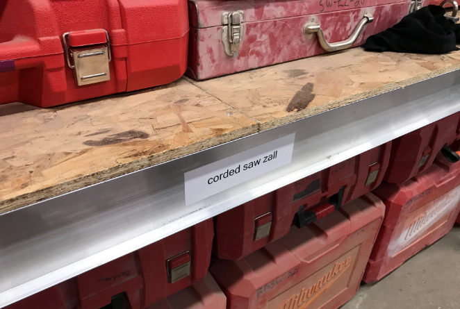 A tool crib is organized with shelving labels indicating tools by category