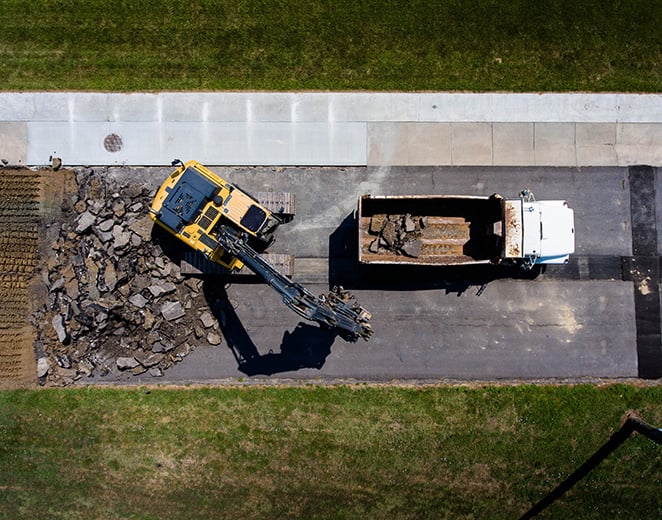 A construction crane empties street debris into a trailer
