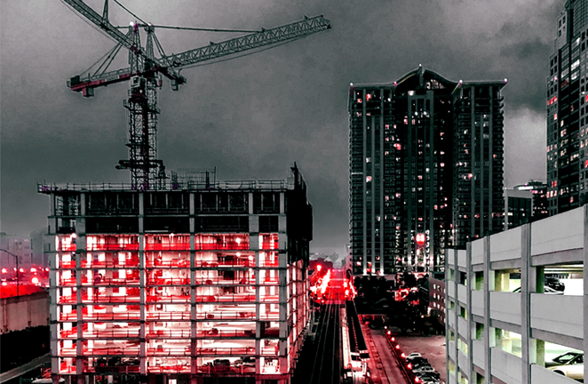 A construction site of a high rise is lit up at night in a city's downtown