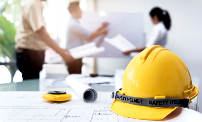 Hard hat on table next to two men and one woman in meeting outlining building plans on white board