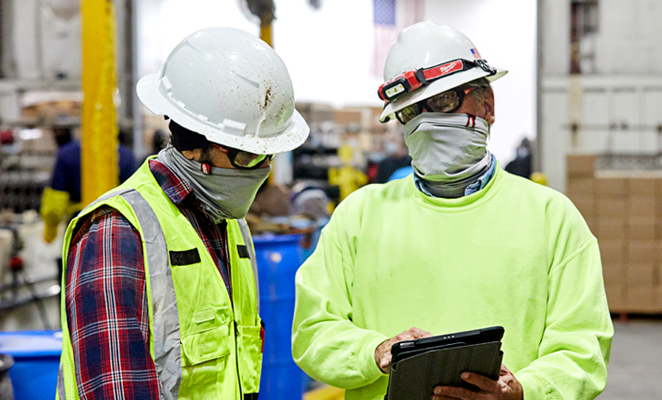 Two consulting construction workers in high visibility yellow apparel and white hard hats view iPad