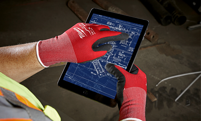 A construction worker on build site wearing red Milwaukee gloves operates BIM software on iPad