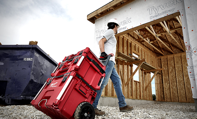 A contractor on a jobsite tows a Milwaukee PACKOUT across gravel into the build site