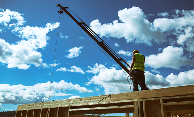 A construction worker in high visibility jacket and yellow hard hat oversees installation of prefabricated walls