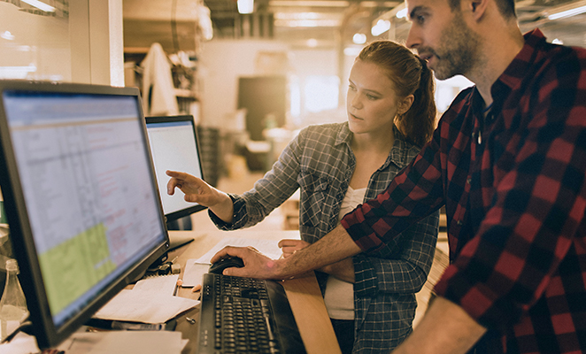 Two young computer specialists review spreadsheets on computer