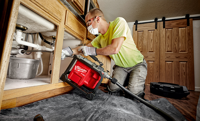 A plumber clears a kitchen sink drain utilizing a Milwaukee sectional drain cleaner