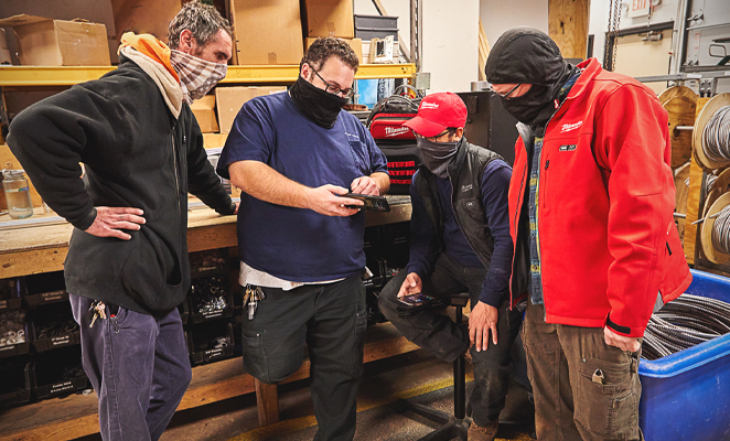 A tool team wearing face masks huddled around smartphone inspecting inventory