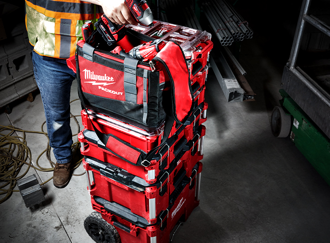 A construction tradesman holds a Milwaukee drill above a PACKOUT tool kit stack 