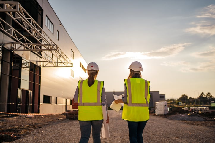 Two women in high visibility vests and hard hats walk on construction jobsite