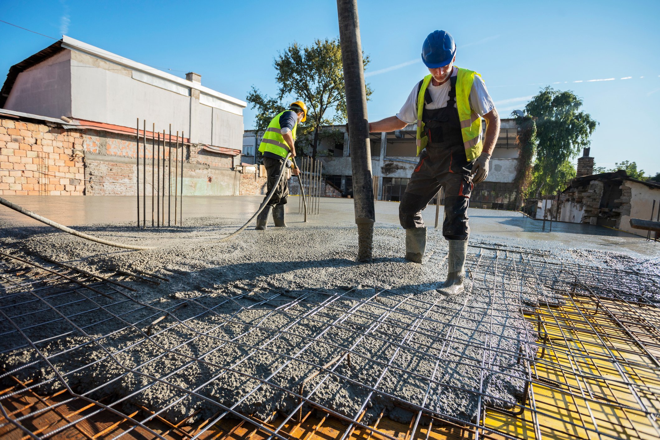 Two concrete masons lay down slab in lot beside commercial business