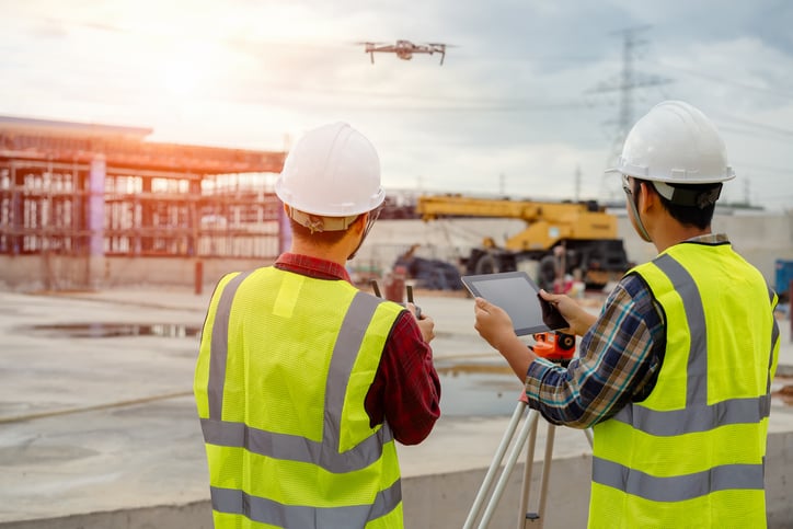 Two construction workers operate drone and review jobsite