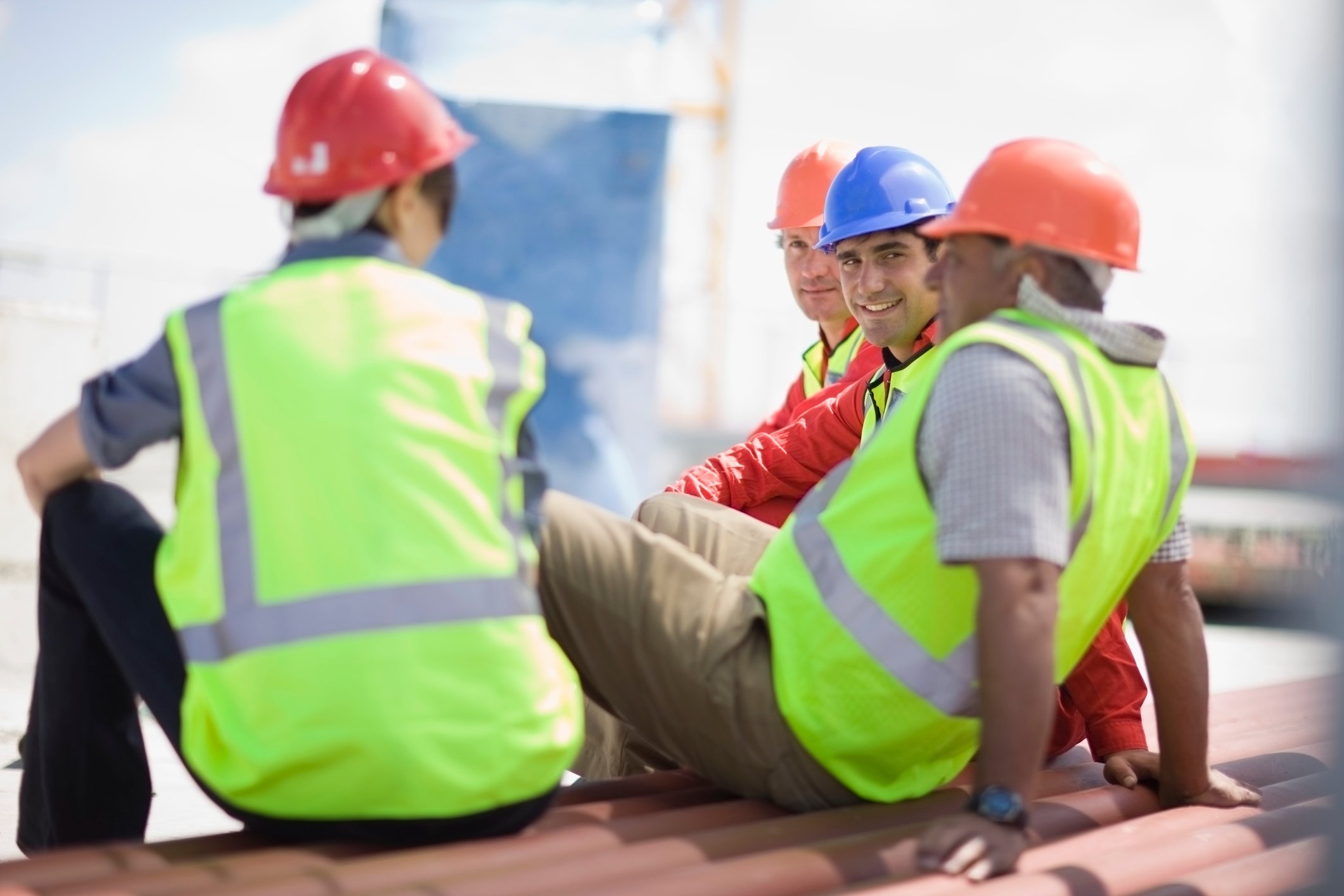 4 construction workers sitting atop roof talking among themselves