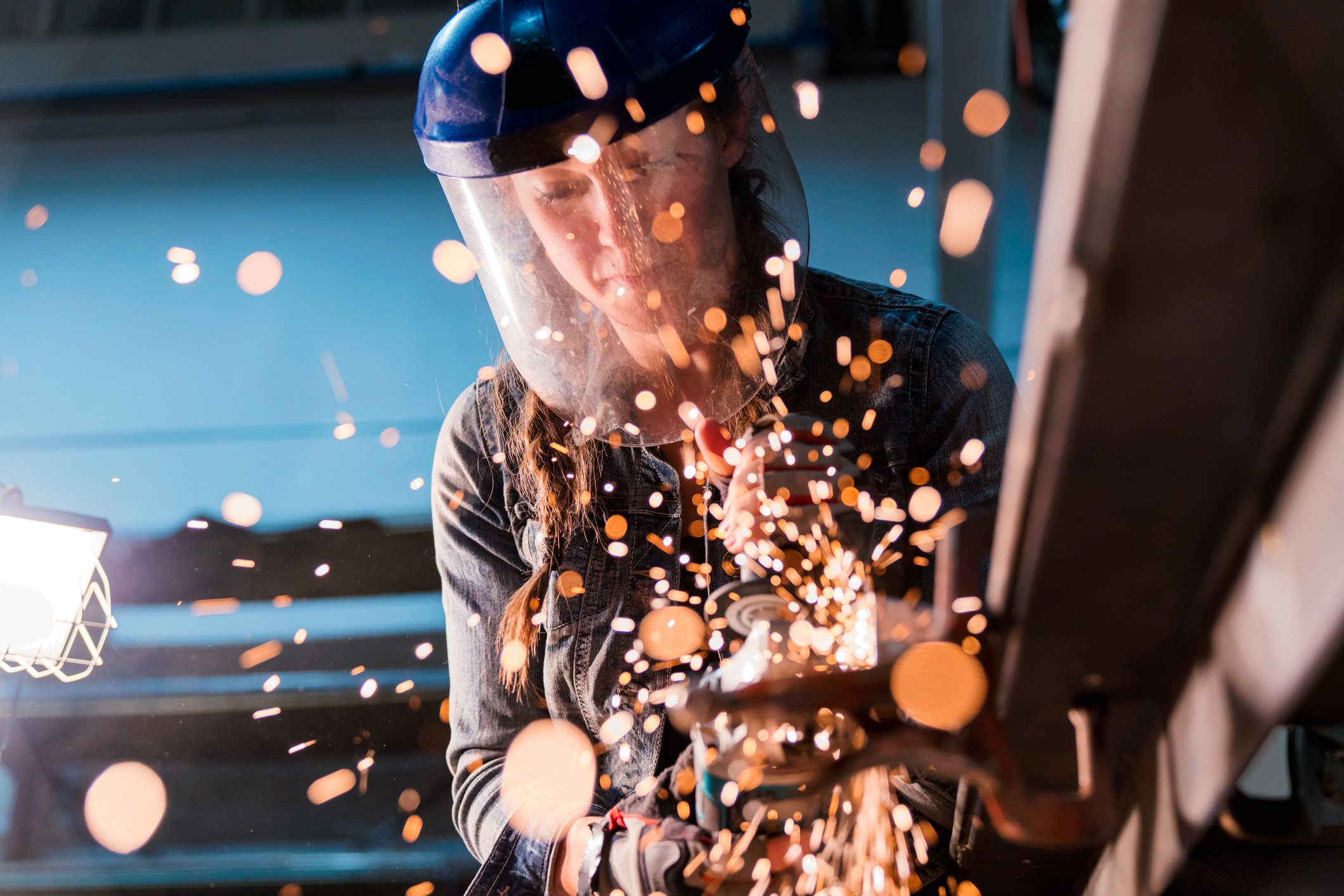 A female metalworker uses grinder tool, illuminating the foreground in flickering sparks 