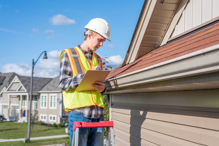 A home inspector examines shingles on roof