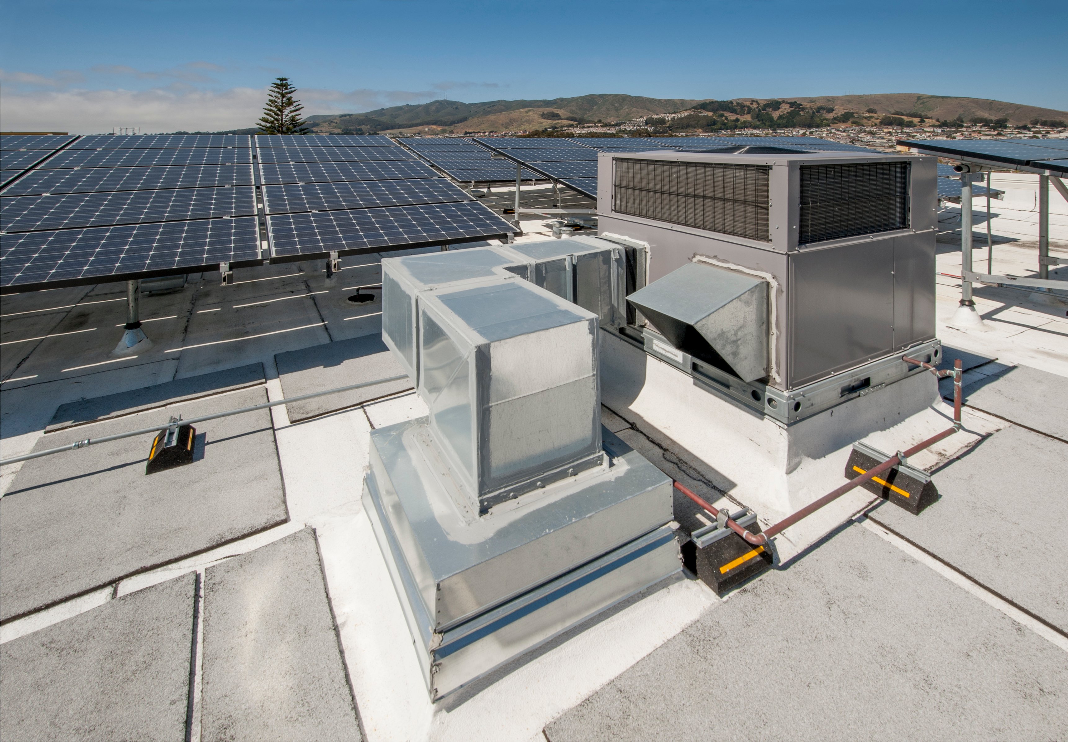 A commercial HVAC system on roof beside rows of solar panels