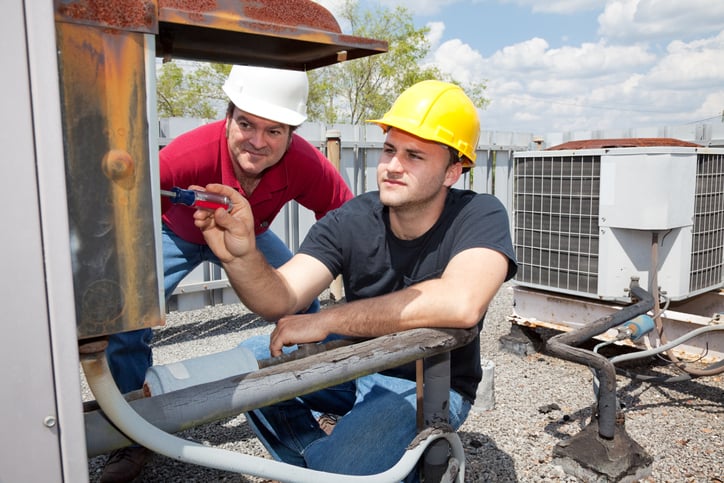 HVAC technician oversees apprentice install AC unit