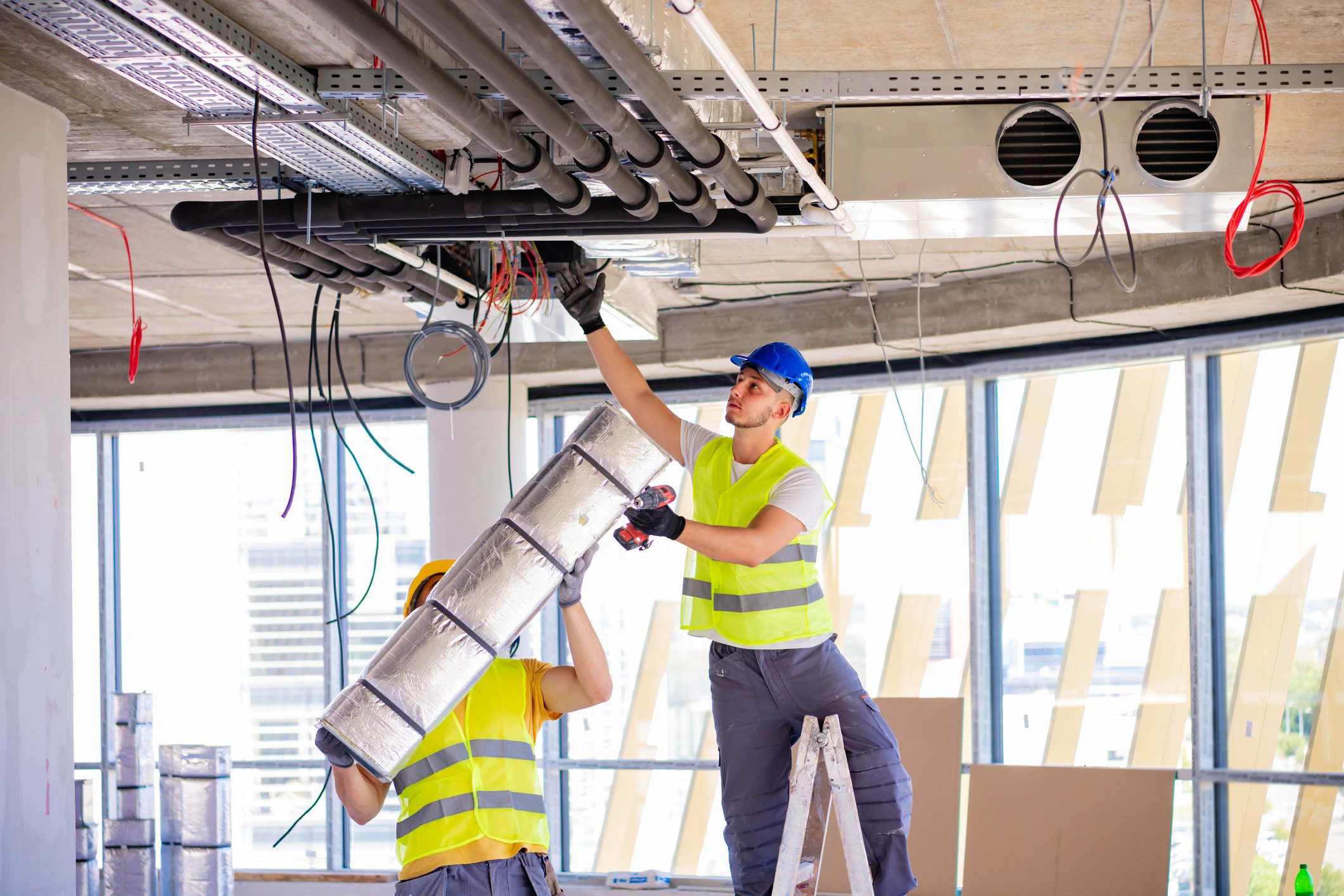 Two HVAC technicians installing overhead ductwork