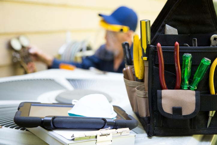 A contractor's tool bag beside tablet device sits atop AC unit