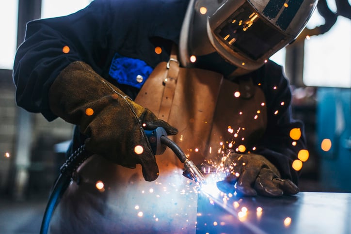 Welder in mask using a cutting torch on a piece of steel.