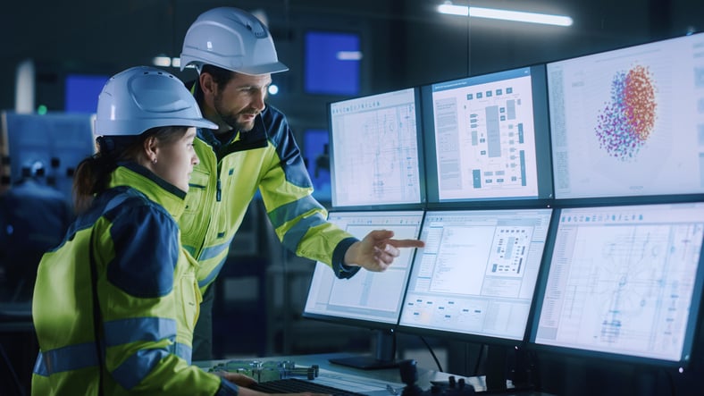 Workers in hard hats viewing computer screens.