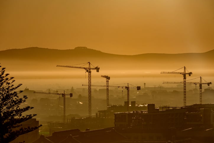 Photo of construction cranes looming in hazy terrain