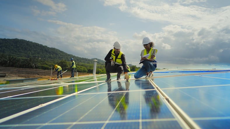 Photo of a and woman in construction hardhats and reflective vests inspecting an array of solar panels.