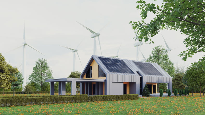 Photo of a home with solar panels on the roof and wind turbines in the background.