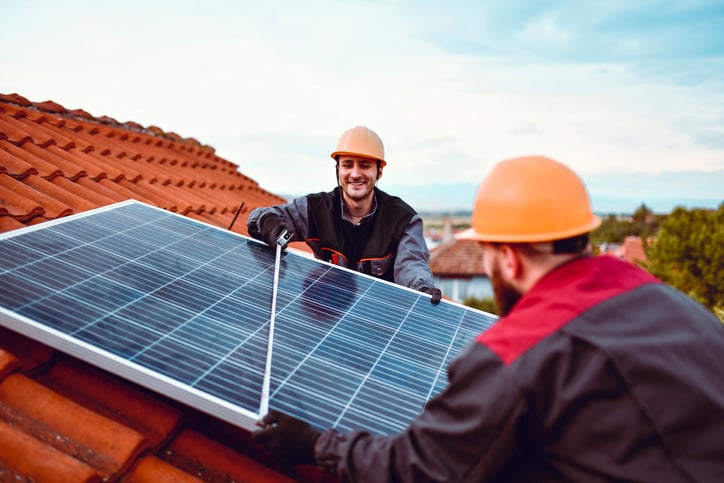 Two tradesmen install a residential solar panel on a homeowner's roof