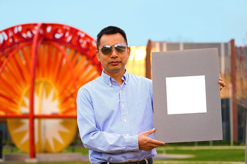 Image of a man holding a poster board with a sample of the whitest paint painted on it.