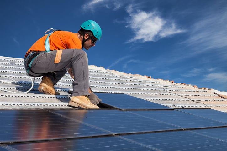 A young Solar Photovoltaic specialist installs solar panels on roof