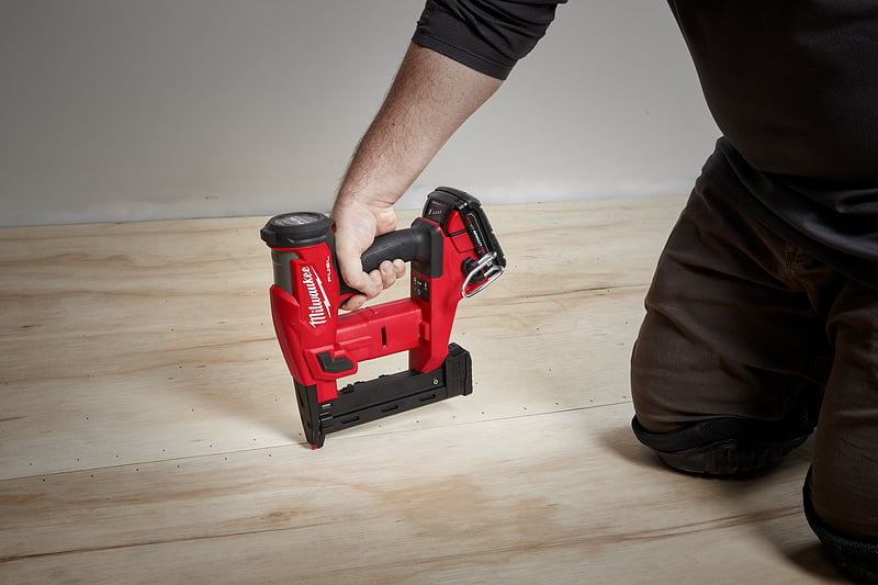 A general contractor uses a staple gun to install flooring