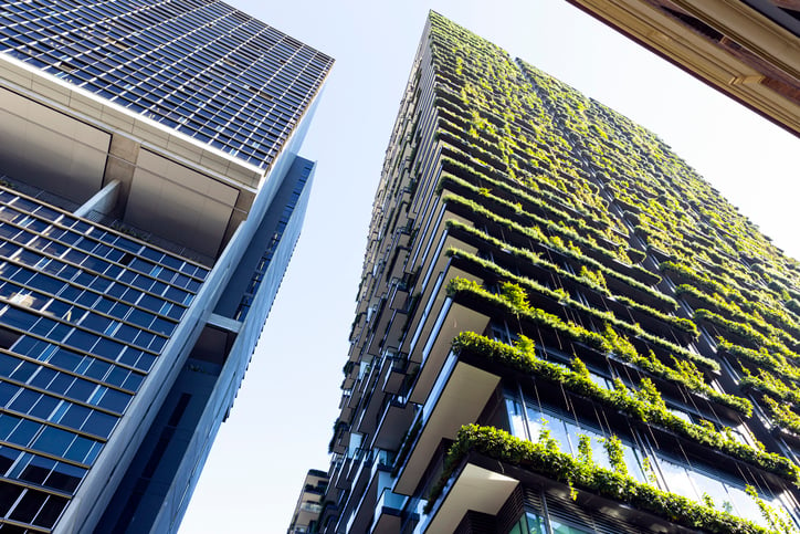 A green building adorned in foliage stands beside a skyscraper