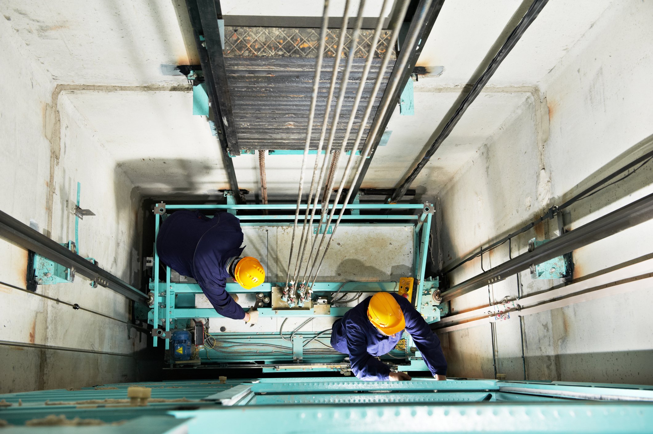 Two service technicians at the bottom of elevator shaft service hydraulics system