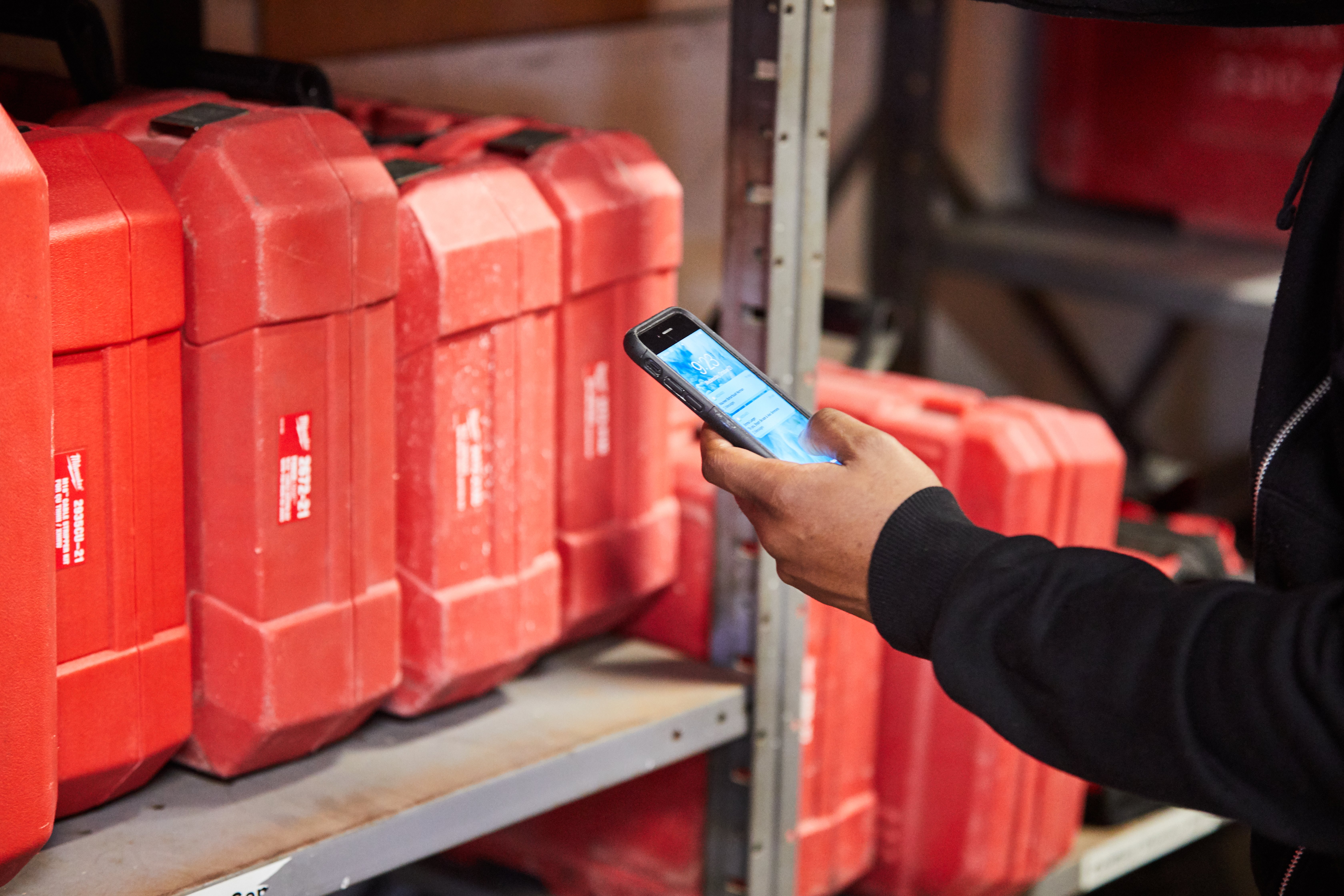 A tool crib manager among inventory shelving uses smartphone