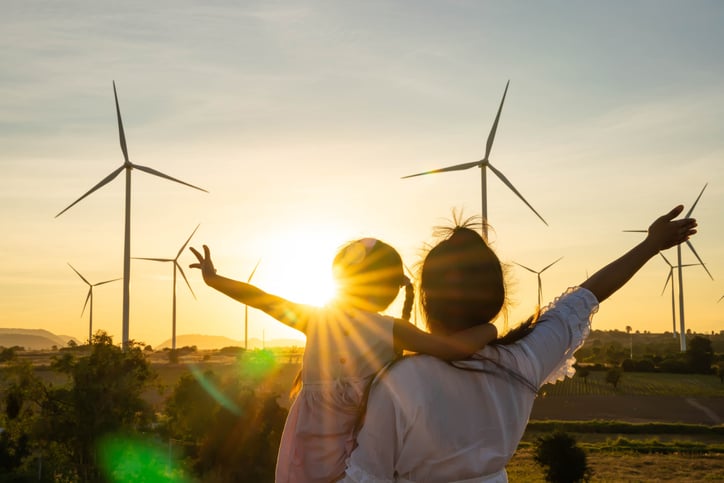 Photograph of a woman and child silhouetted against a sunset with wind turbines in the distance. 