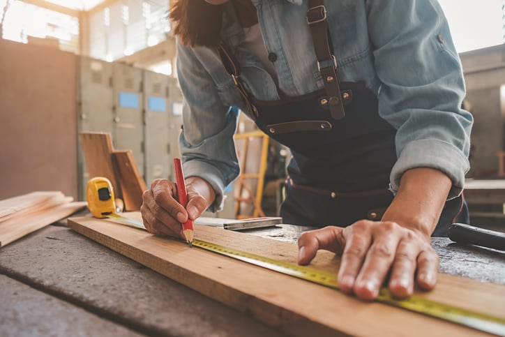 A woodworker measures a piece of plywood with a tape measure