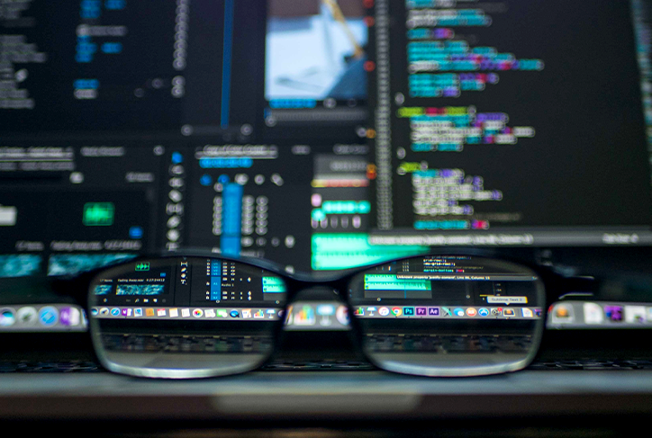 Computer monitor displays code, seen through the lens of eyeglasses sitting on a desk