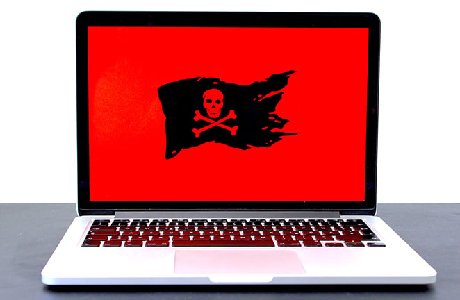 A laptop computer displays red background with black and red pirate flag symbolic of a cyber attack