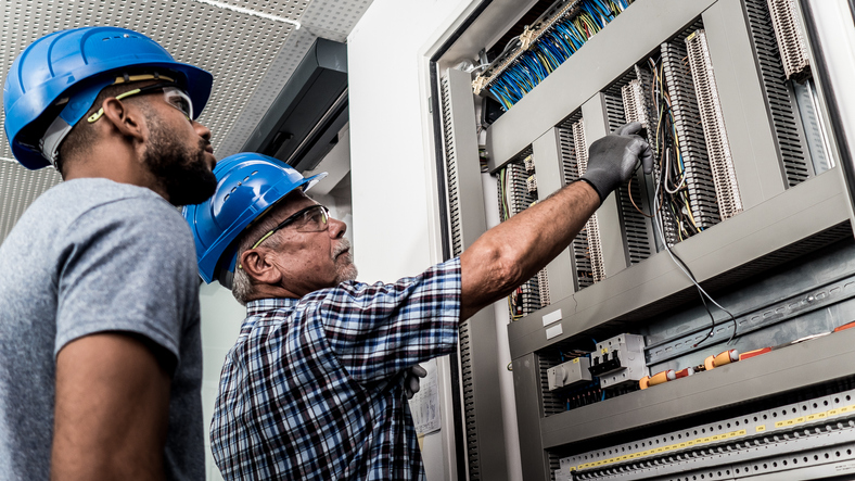 A Master Electrician demonstrates proper wiring to Apprentice