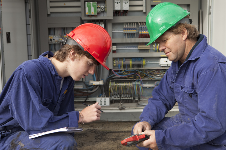 An apprentice learns from a master electrician